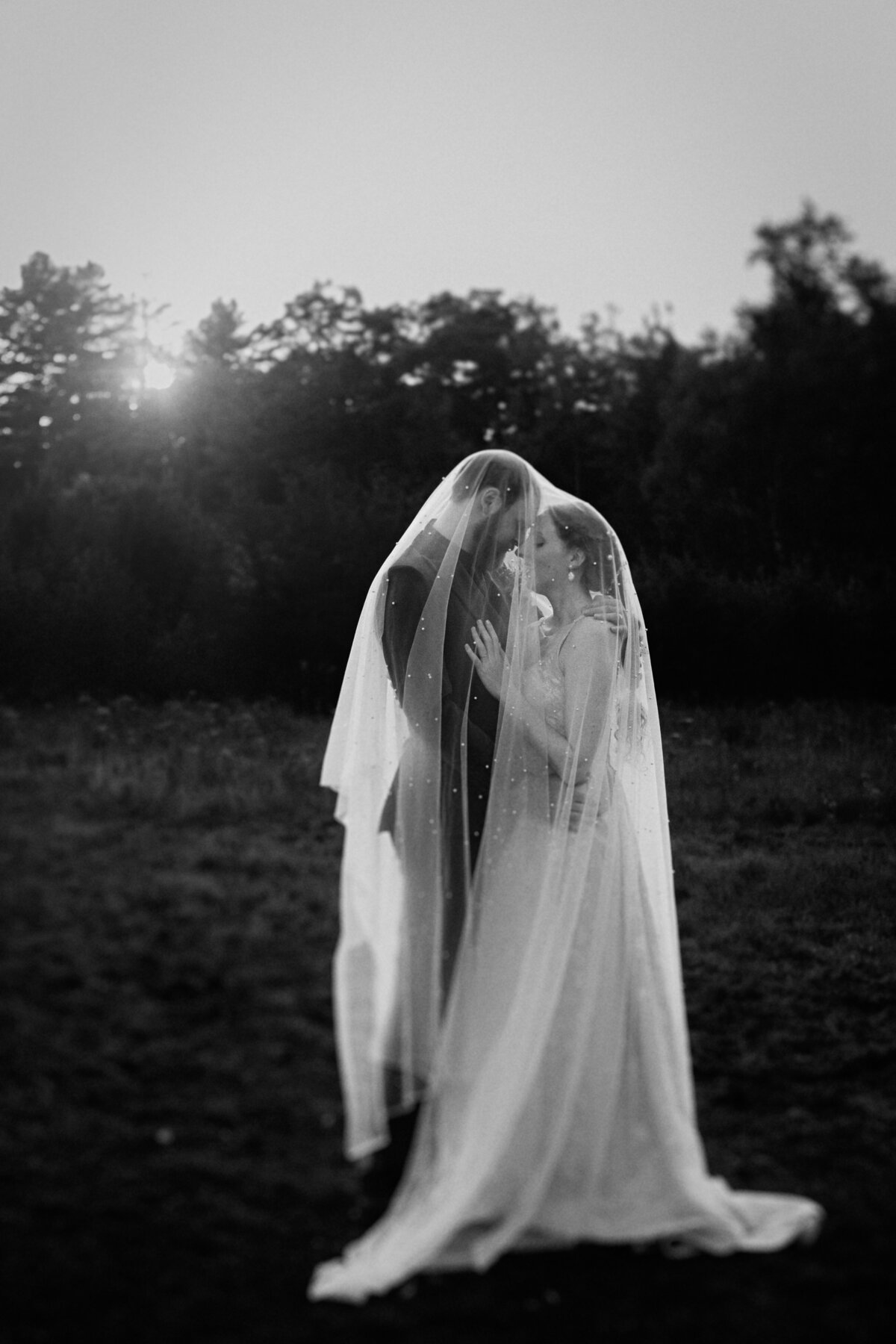 black-and-white-photo-of-a-couple-under-a veil-in-nature-at-sunset-at-camp-eden-woods