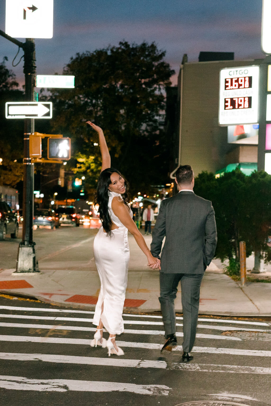bride with on hand up and the other holding grooms hand as they walk across a street