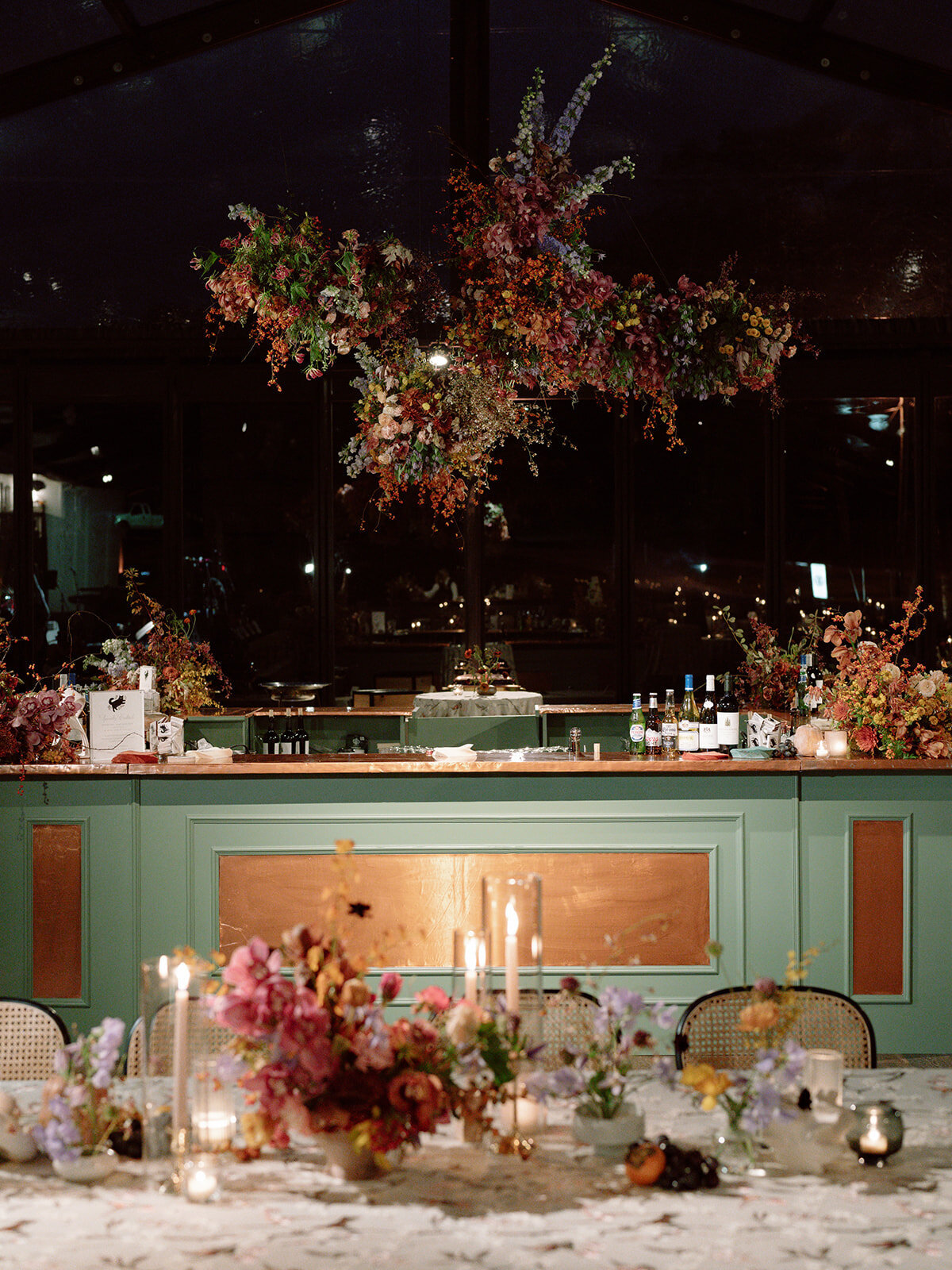 Interacting and sculptural floral clouds hang over the dance floor and bars of this fall wedding reception in Tennessee. Clear top tent build out for fall wedding reception in Tennessee hills.  Product clustered floral clouds in a tasteful fall color palette of copper, ruby, gold, burgundy, rust, and lavender. Orchids, bittersweet berries, butterfly ranunculus, and tulips are highlighted. Unique floral design with flower forward large scale installations. Design by Rosemary & Finch Floral Design in Nashville, TN.
