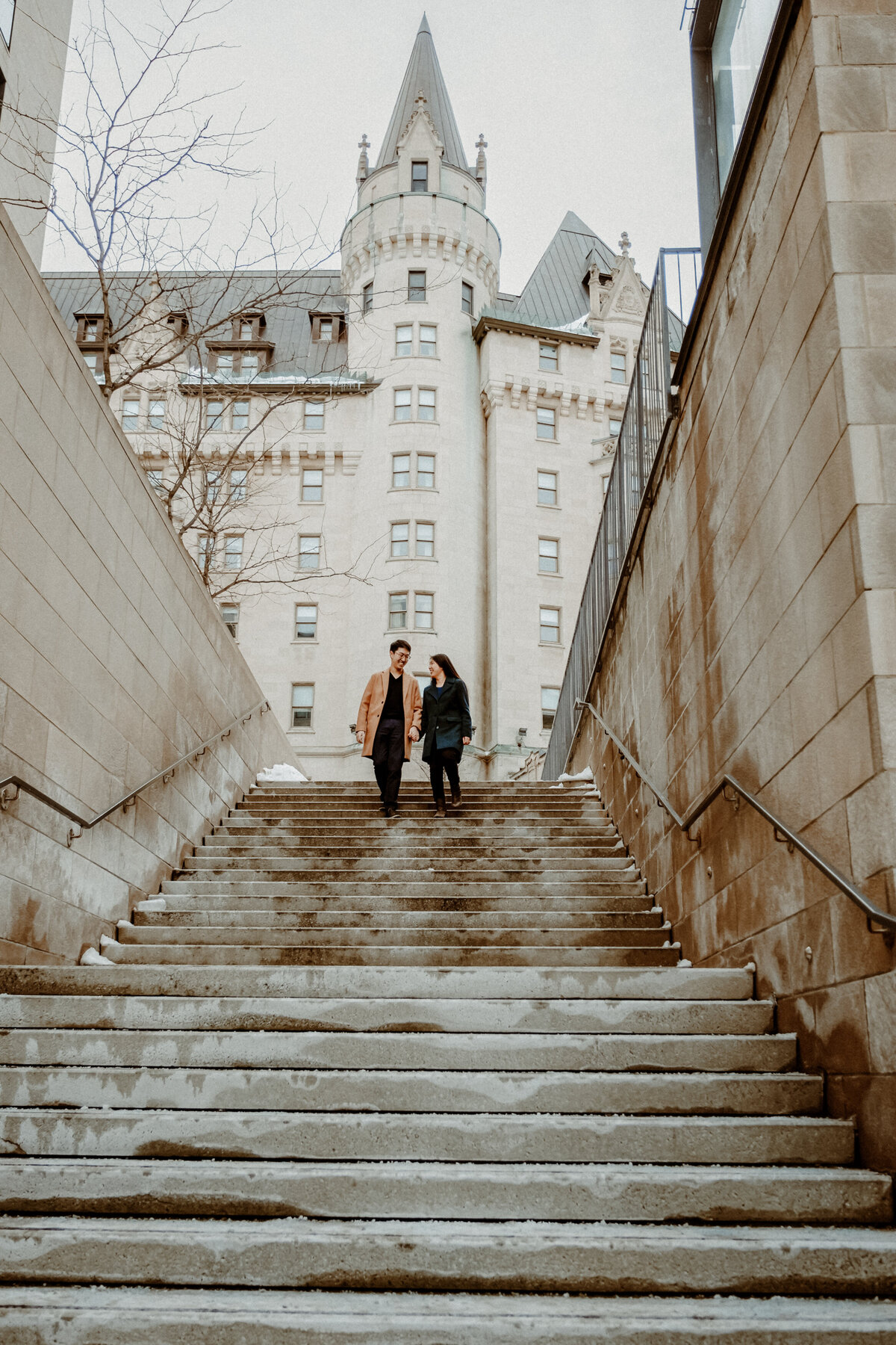 engaged-couple-walking-down-the-stairs-in-front-of-the-chateau-laurier-1