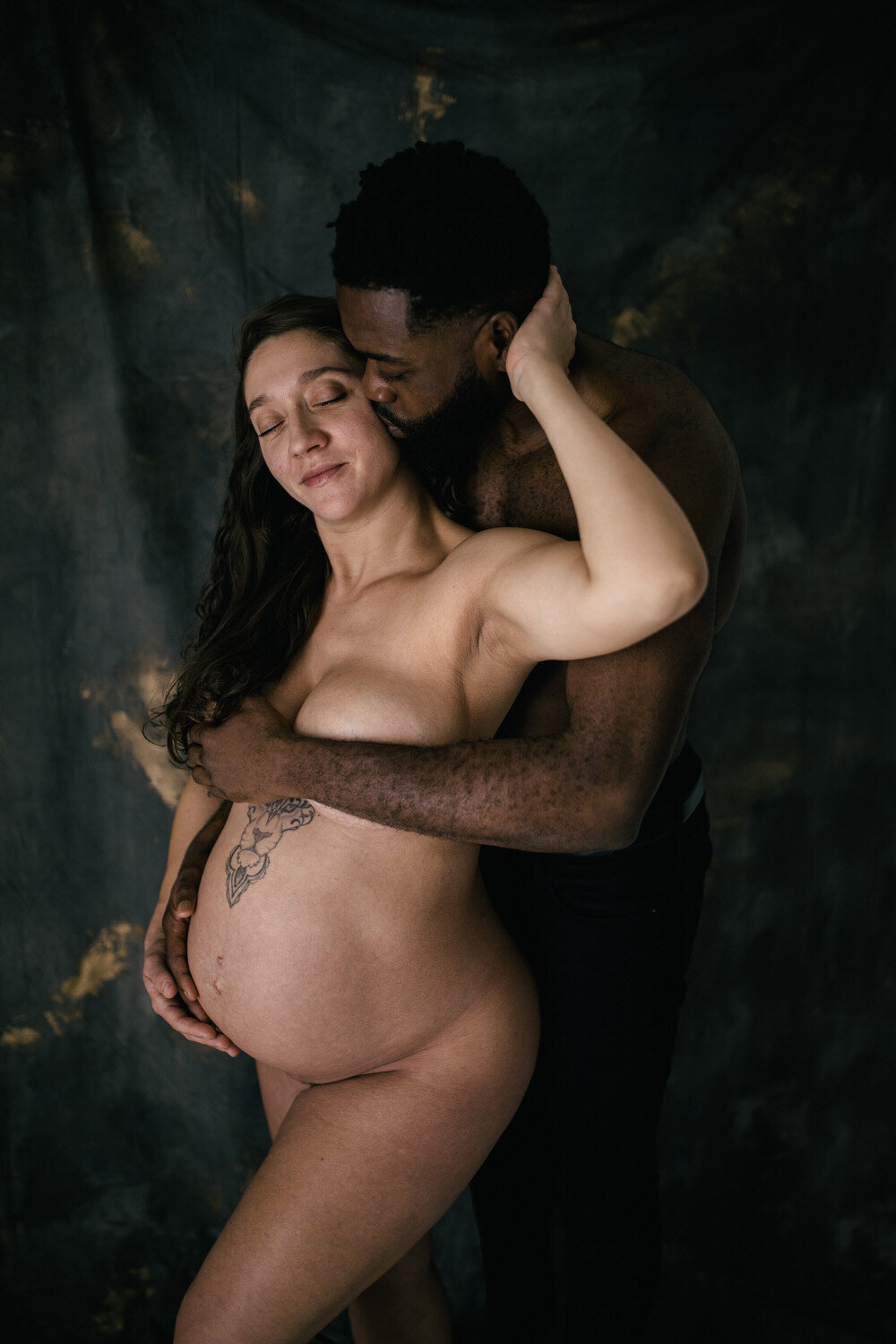 White pregnant women stands infront of her partner and he holds her belly