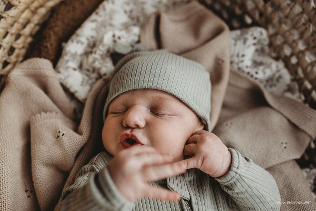 Peaceful slumber of a newborn baby in a grey knit outfit and hat, resting in a rustic basket with layers of soft fabric. Ruaa Hamdan Photography