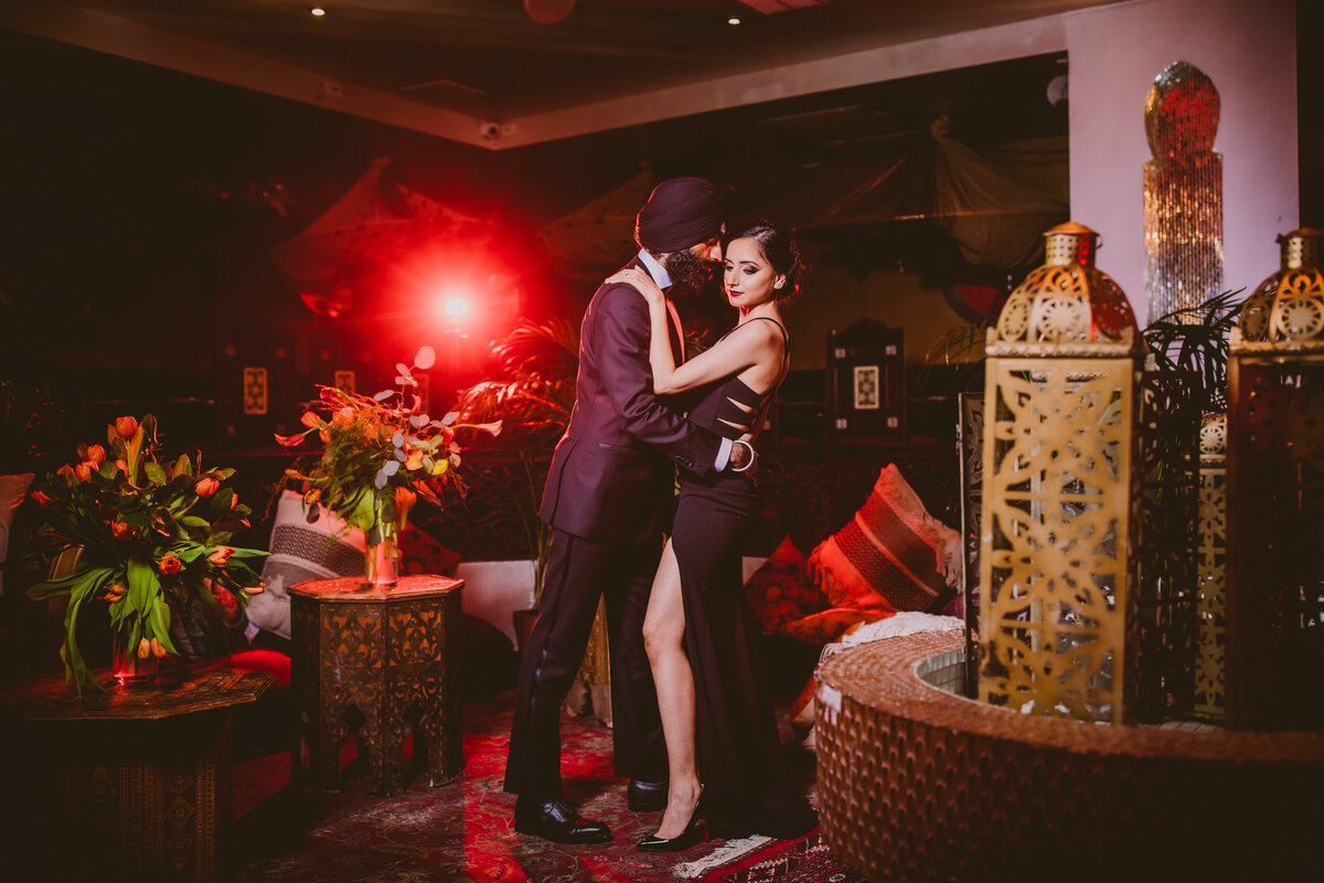 An engaged couple in black formal clothing inside a restaurant lounge indoors in a dark intimate setting, bond themed