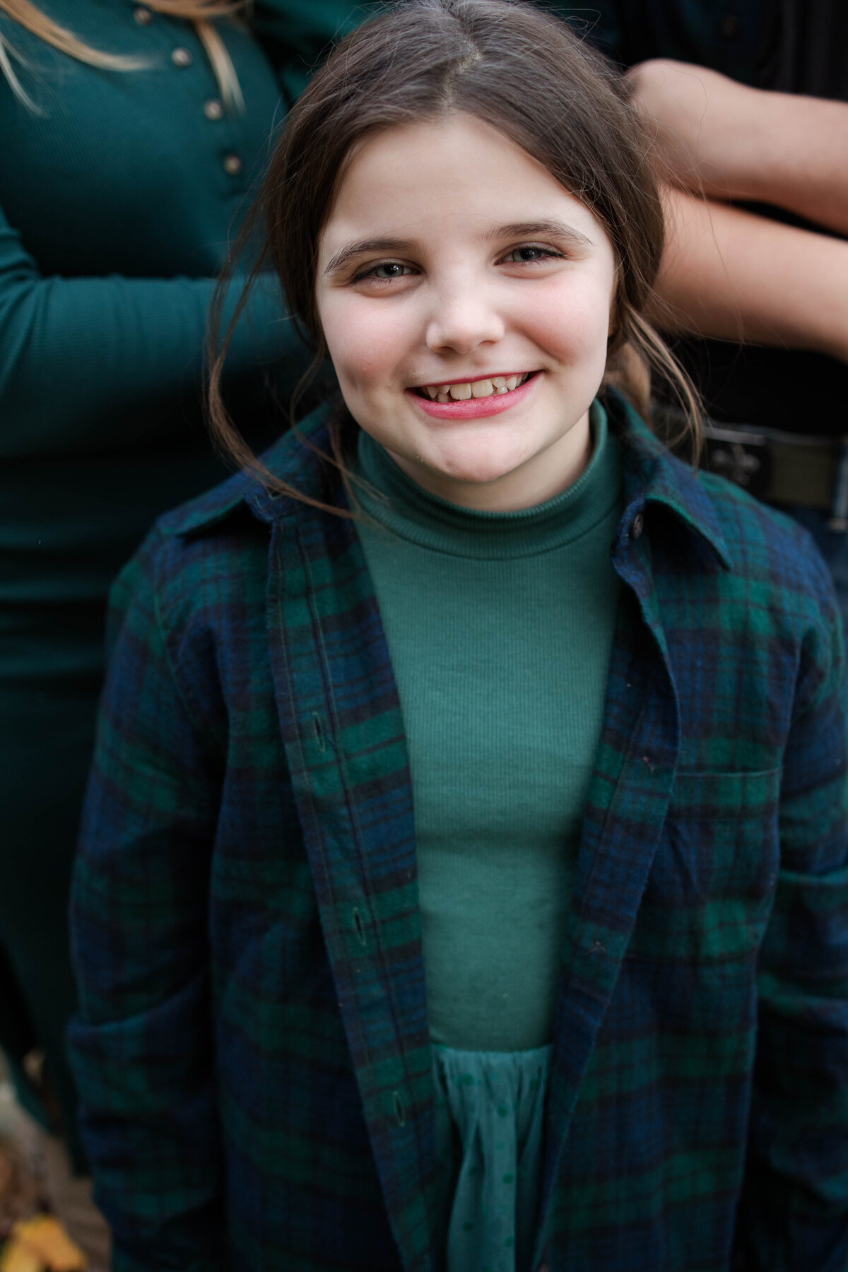 young girl smiling while wearing a green dress and blue and green flannel