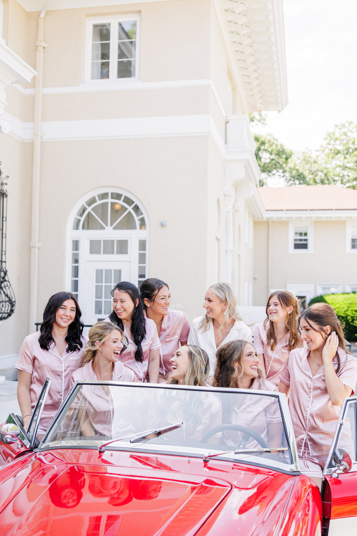 Bride and bridesmaids laughing while sitting in a vintage car at Tupper Manor