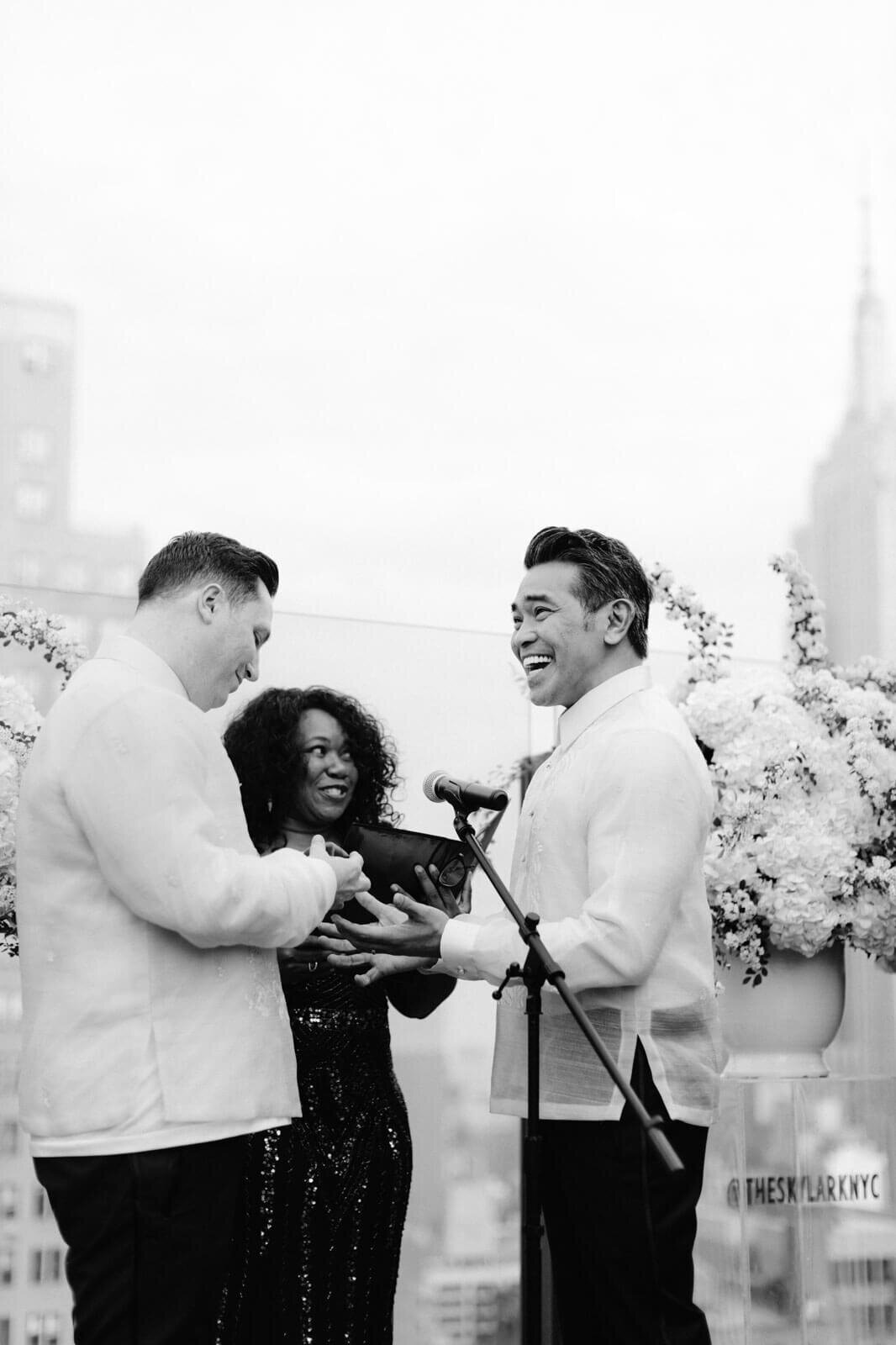 Two grooms are smiling during a wedding ceremony in The Skylark, New York. Wedding Image by Jenny Fu Studio