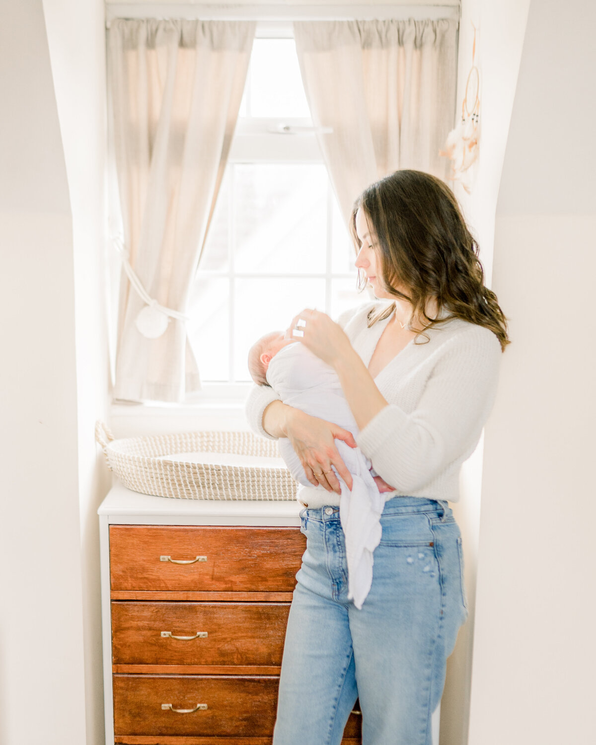 Mother cradling newborn baby in a nursery by Oklahoma City Newborn Photographer Courtney Cronin