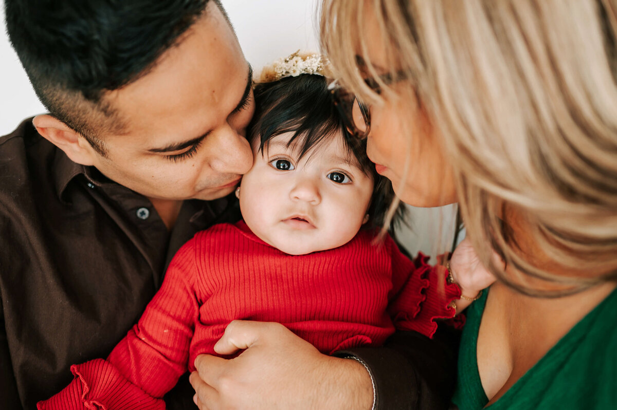 Branson family photography of parents kissing baby girl in red