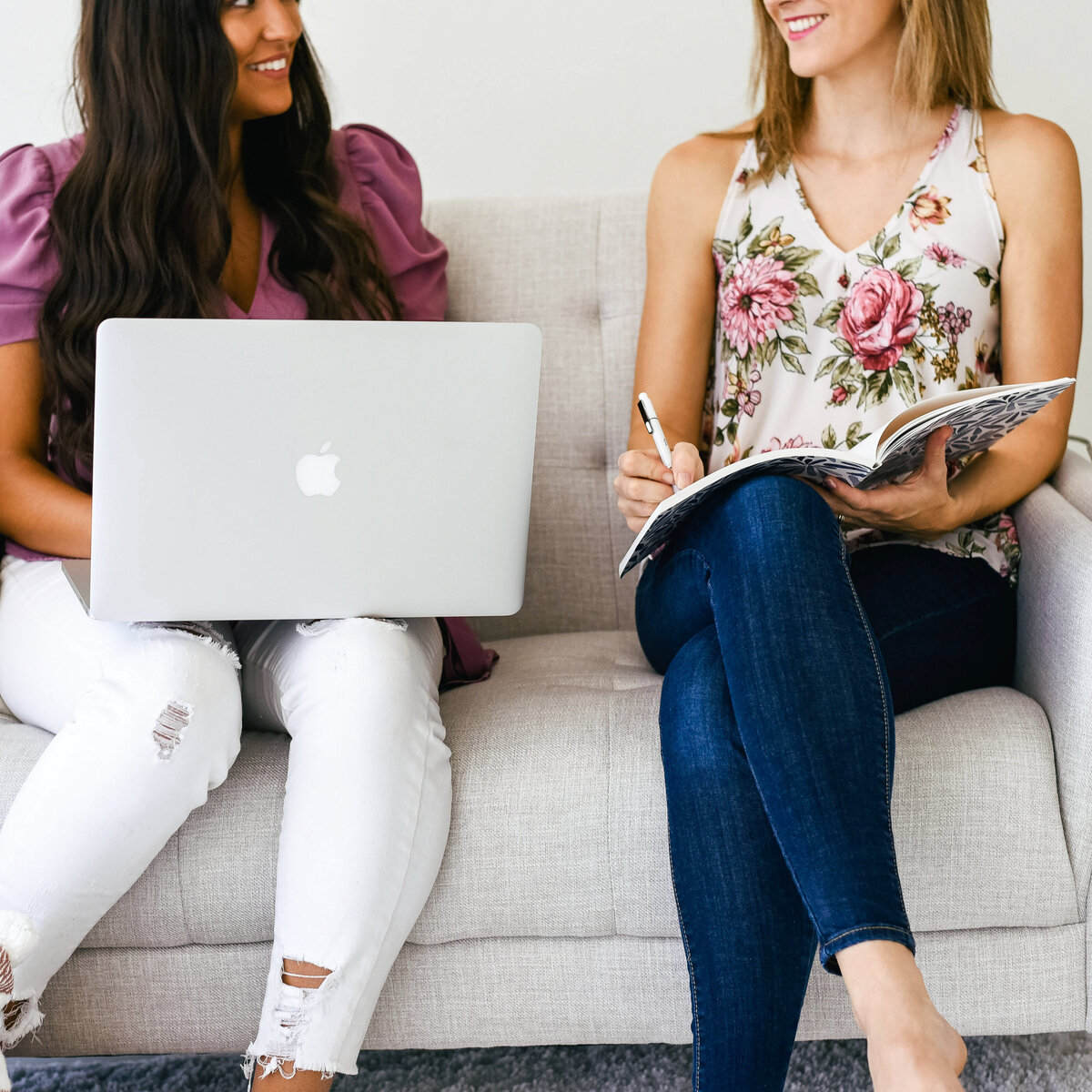 Two females on a couch with a laptop and writing in an notebook