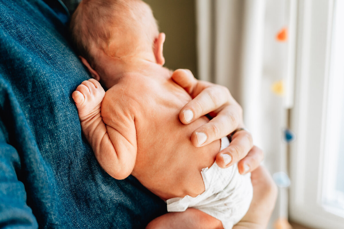 A close-up shot of a newborn baby resting against a parent’s chest, showcasing the baby’s small, delicate body and the parent's gentle embrace.