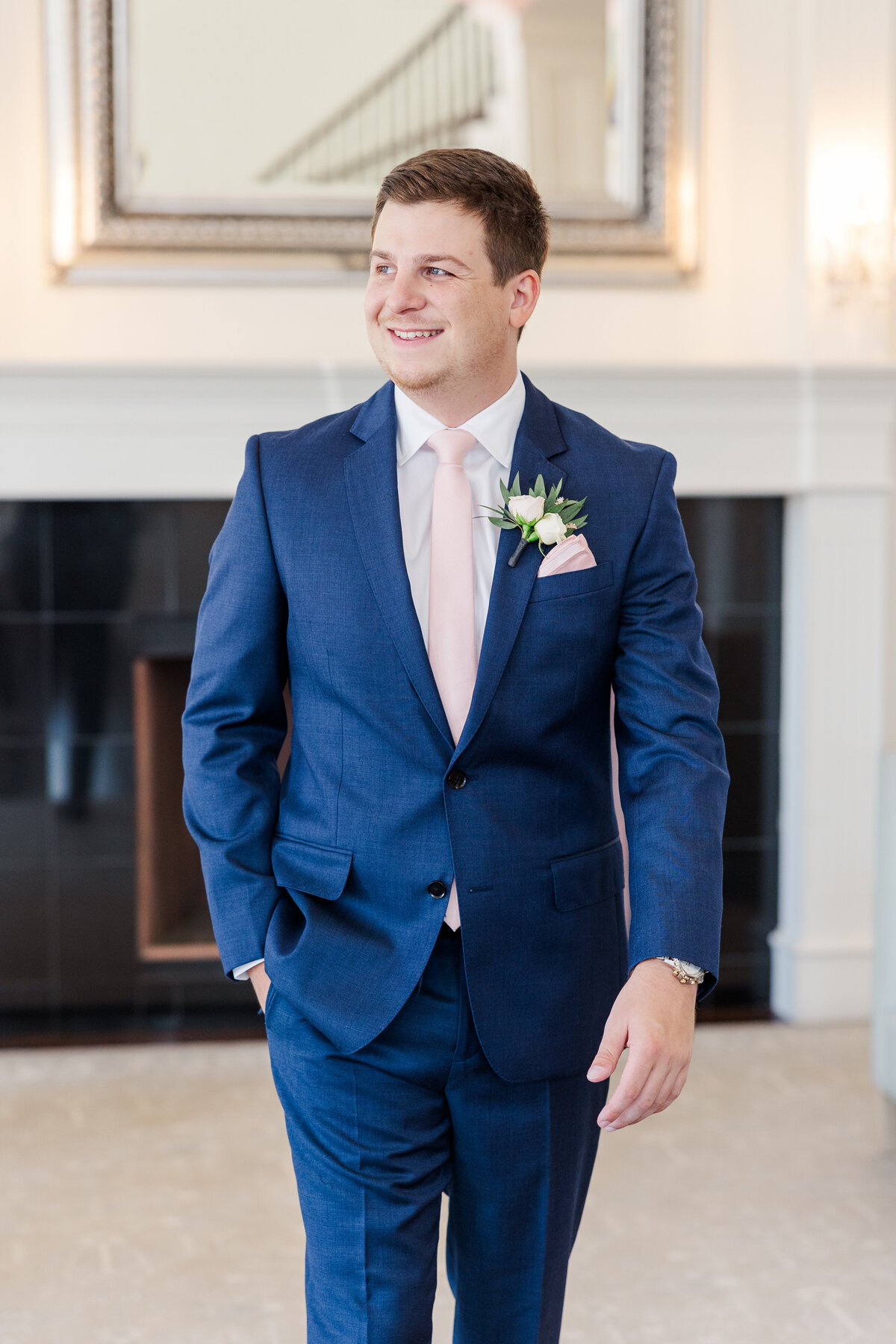 An elegant groom stands confidently in a navy suit and blush tie, captured in a bright, natural light setting with timeless, clean composition. Ideal for couples planning weddings near Flower Mound, Plano, or Highland Village who value light and airy photography with a refined, classic feel.