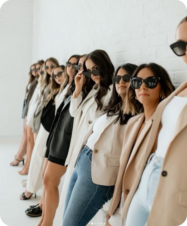 Numerous women leaning against a white brick wall to portray community and connectivity during a brand photoshoot for social media. 