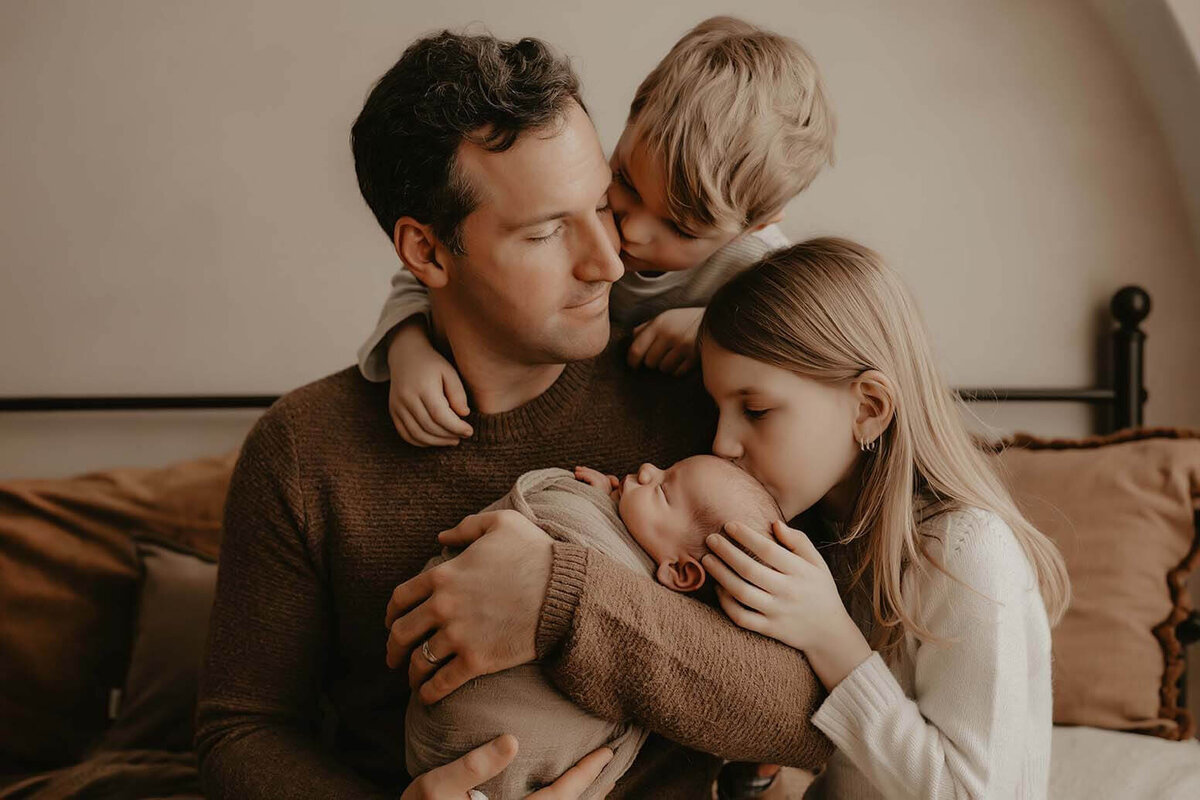 A dad holding his new son while his two other children kiss the baby and the dad in rochester ny