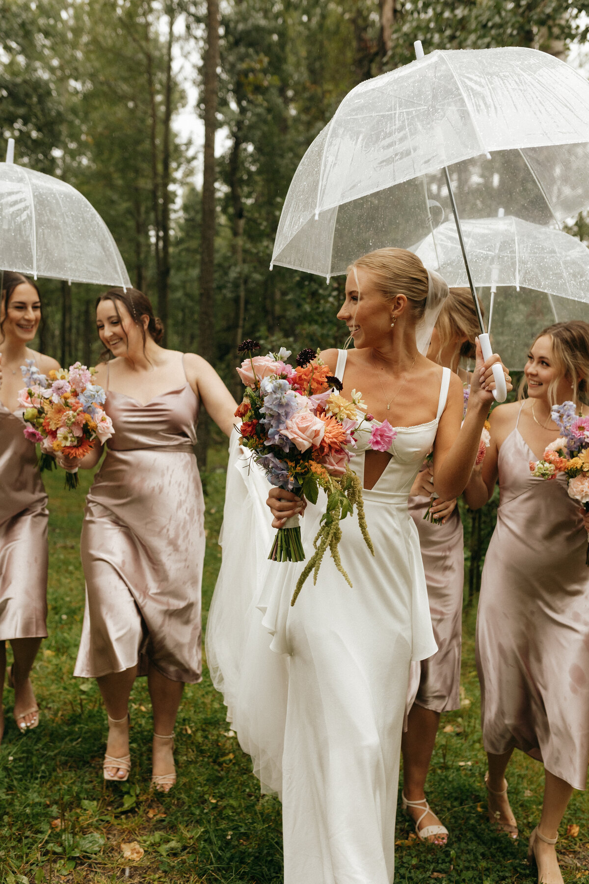 An August bride with her bridesmaids holding umbrellas, smiling at each other