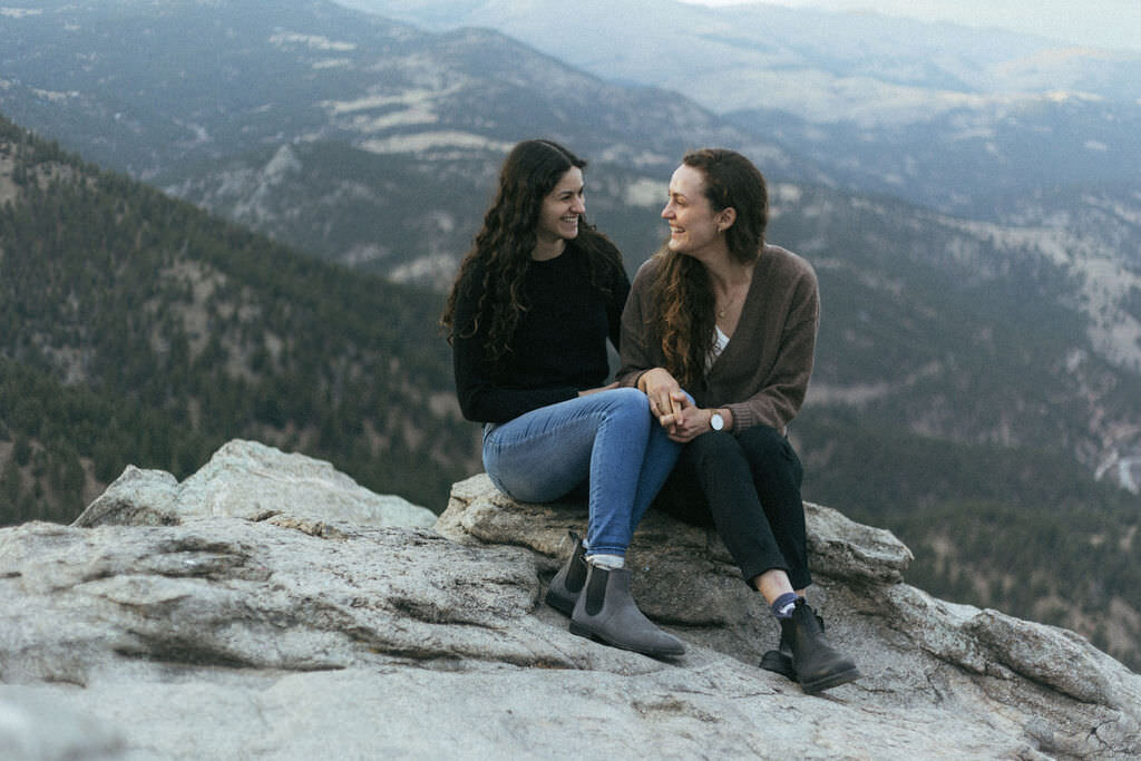 A couple sitting on a rock overlooking a mountain.