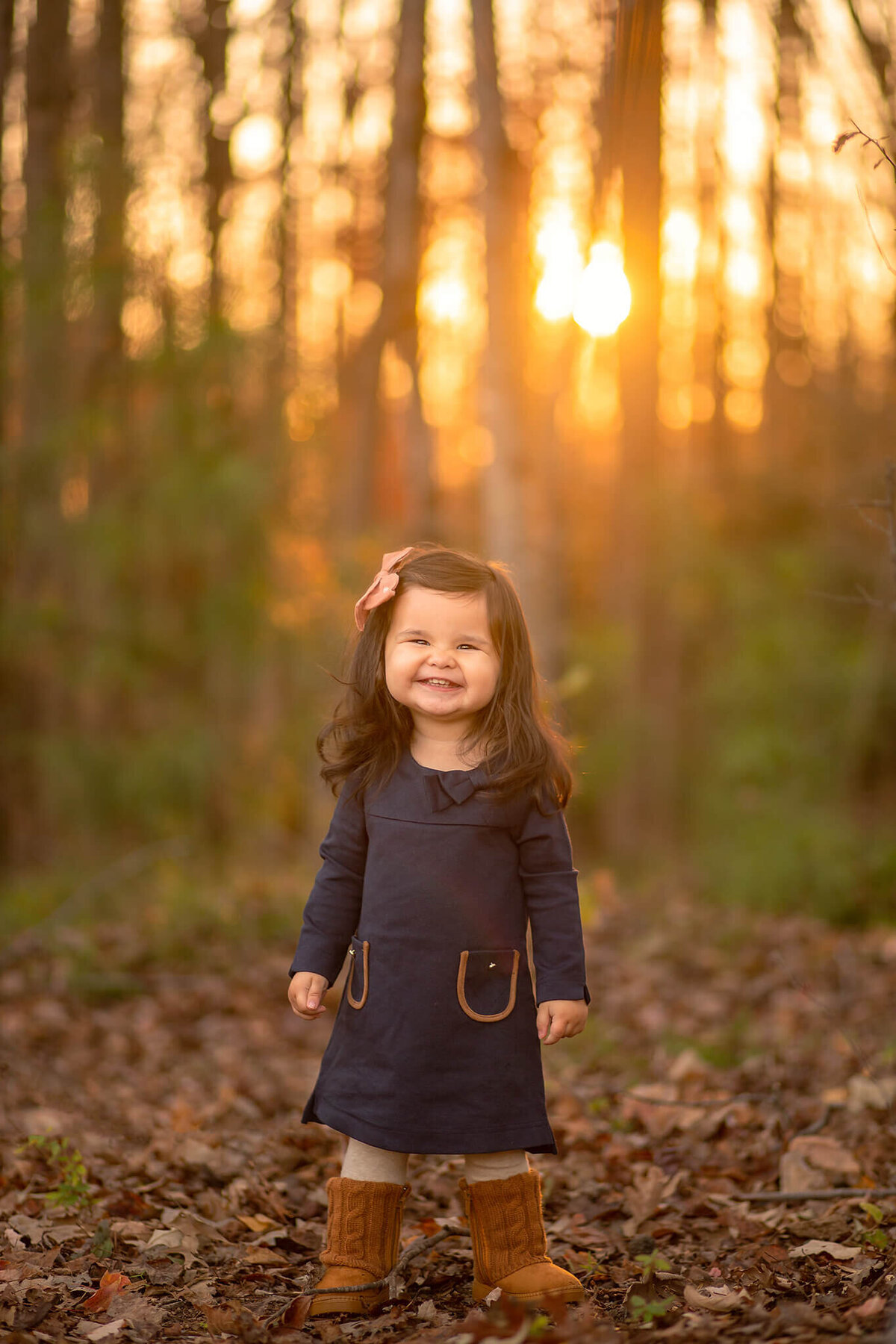 Little girl smiling in the leaves at sunset at Forest Ridge Park by Susan VanNess Photography, a Raleigh children's photographer