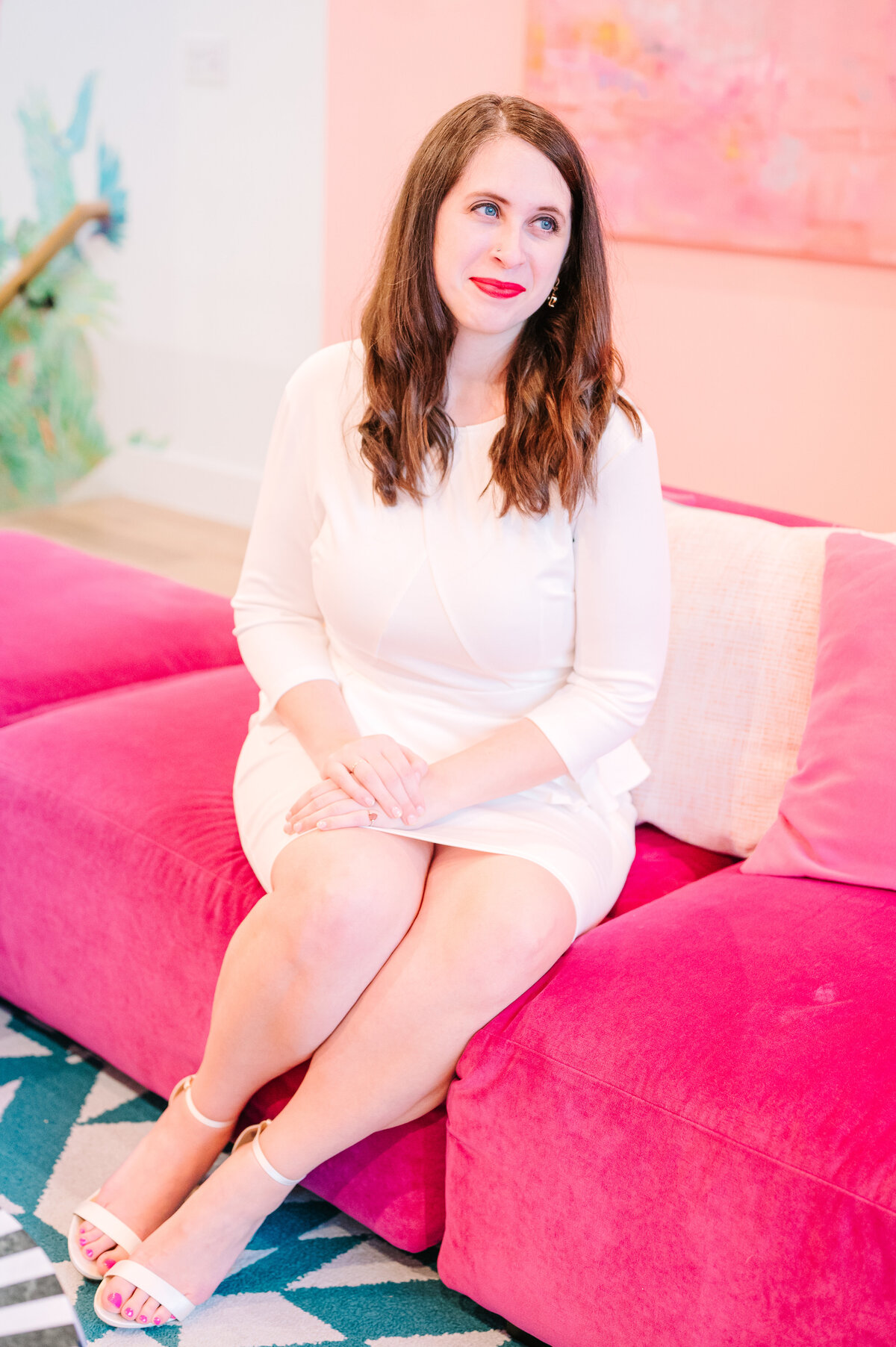 Cait Potter smiling in a white outfit on a pink sofa
