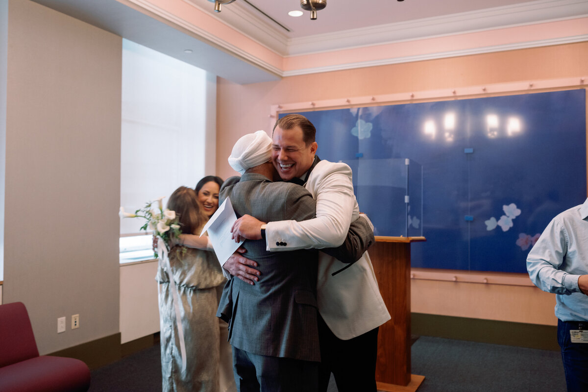 Chris embraces a family member with a big smile while Japna hugs a loved one after their NYC City Hall wedding ceremony