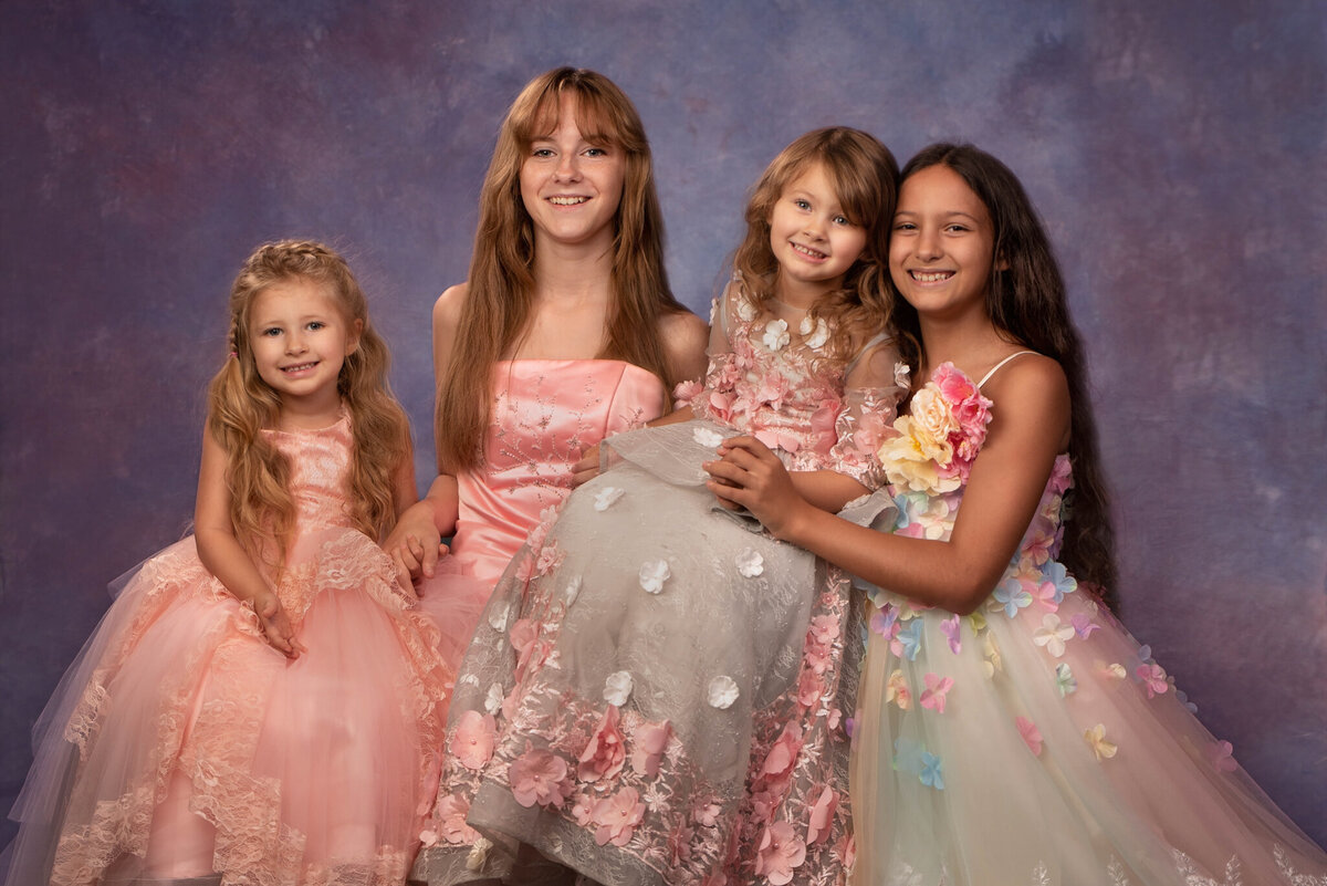 Elegant studio portrait of three sisters in stunning pink and white gowns, captured in Overland Park, Kansas. Perfect for families seeking timeless and formal sibling photography in the Kansas City metro area.