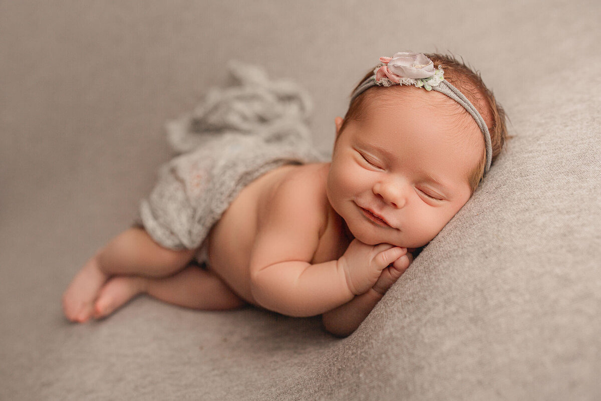 newborn baby on grey backdrop smiles for the camera during her Hamilton, ON newborn photography session