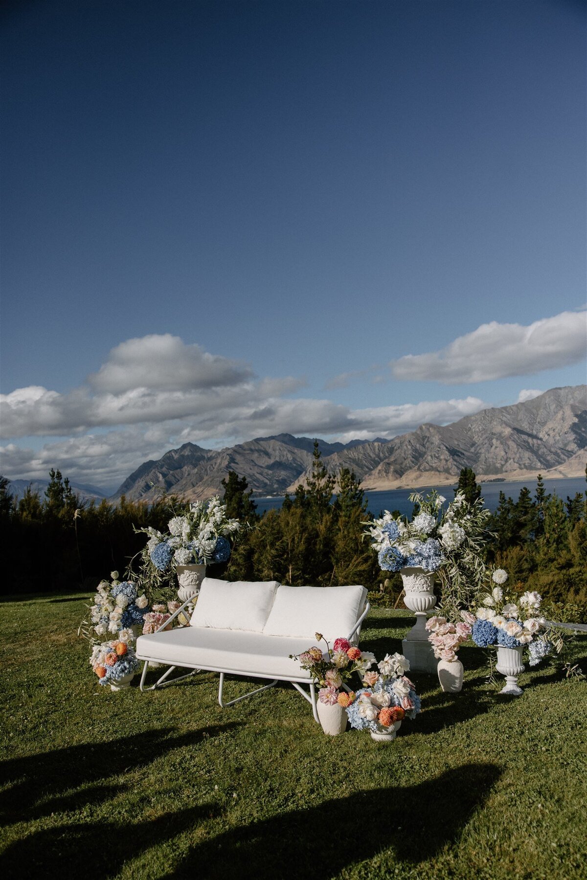 Lounge seating area styled with vibrant florals and mountain views for an alfresco ceremony celebration overlooking Lake Hāwea.