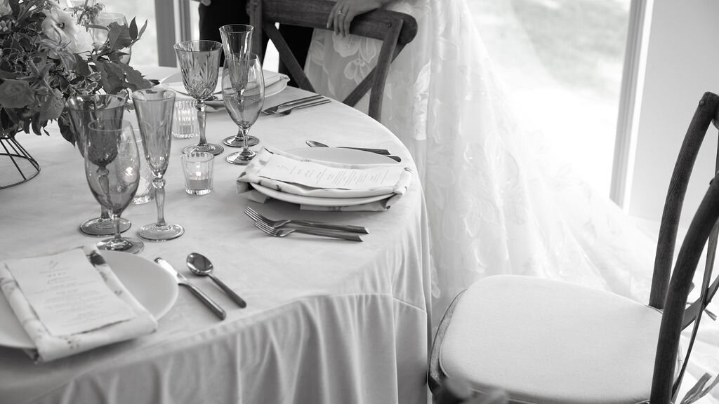 black and white image of a beautiful table with velvet tablecloth and fine china with a bride and groom standing nearby in the Willowbrook wedding venue in Pittsburgh