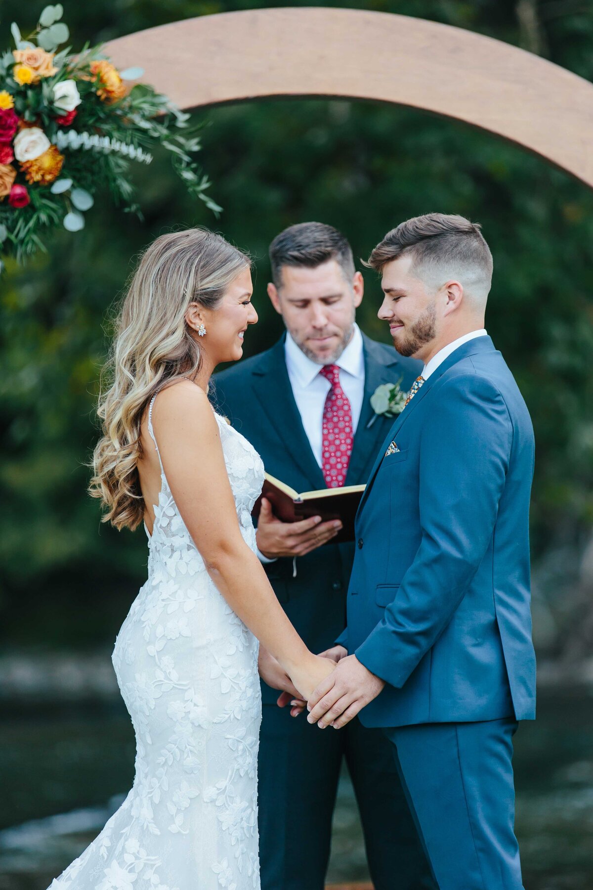 Bride and groom holding hands at crooked river wedding arbor