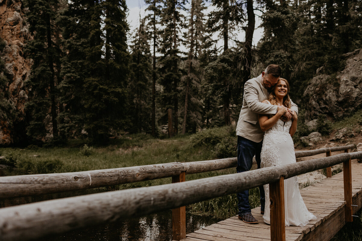 groom hugging his new bride from behind on a outdoor bridge
