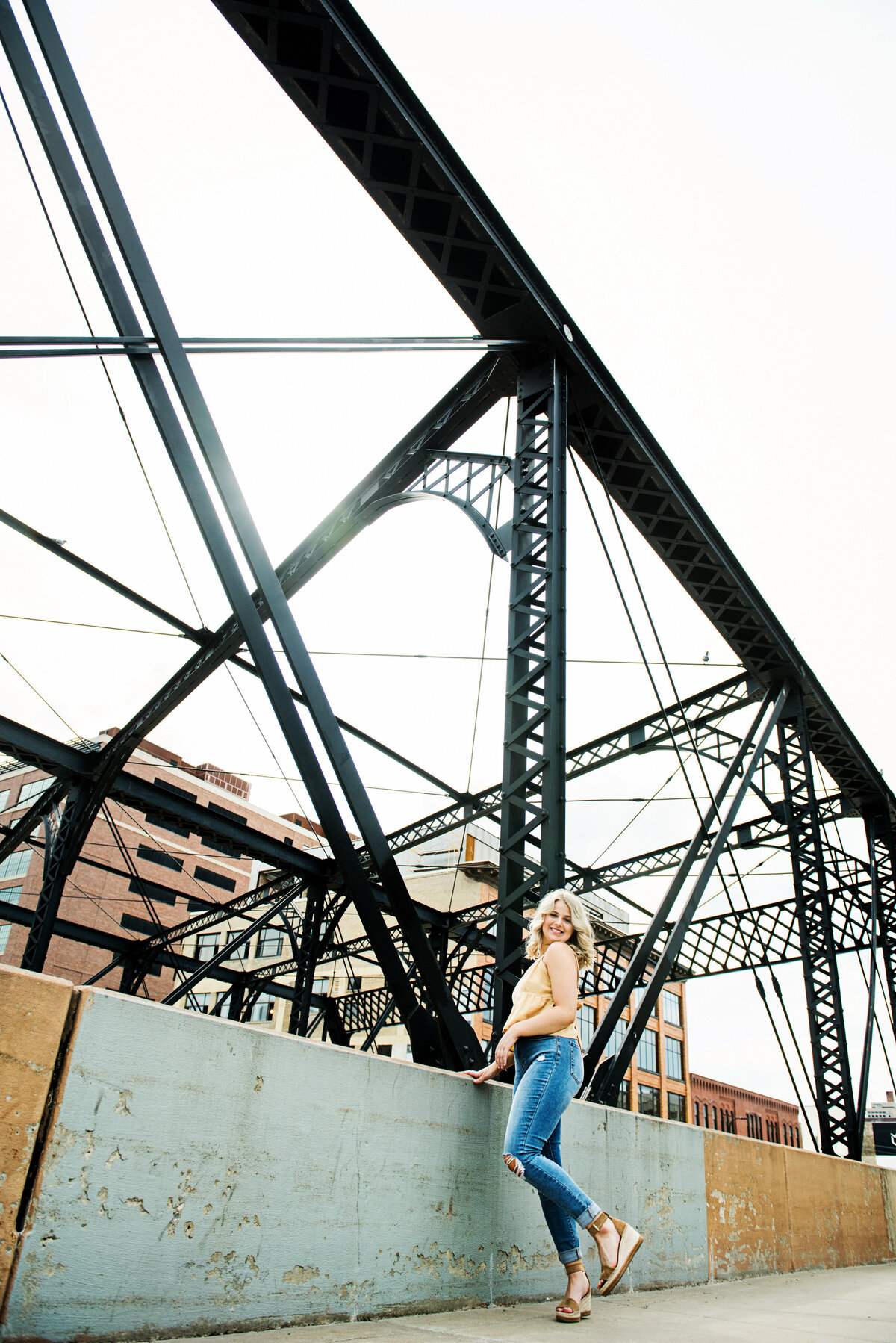 high school senior photo of girl in street fashion leaning against old railroad bridge