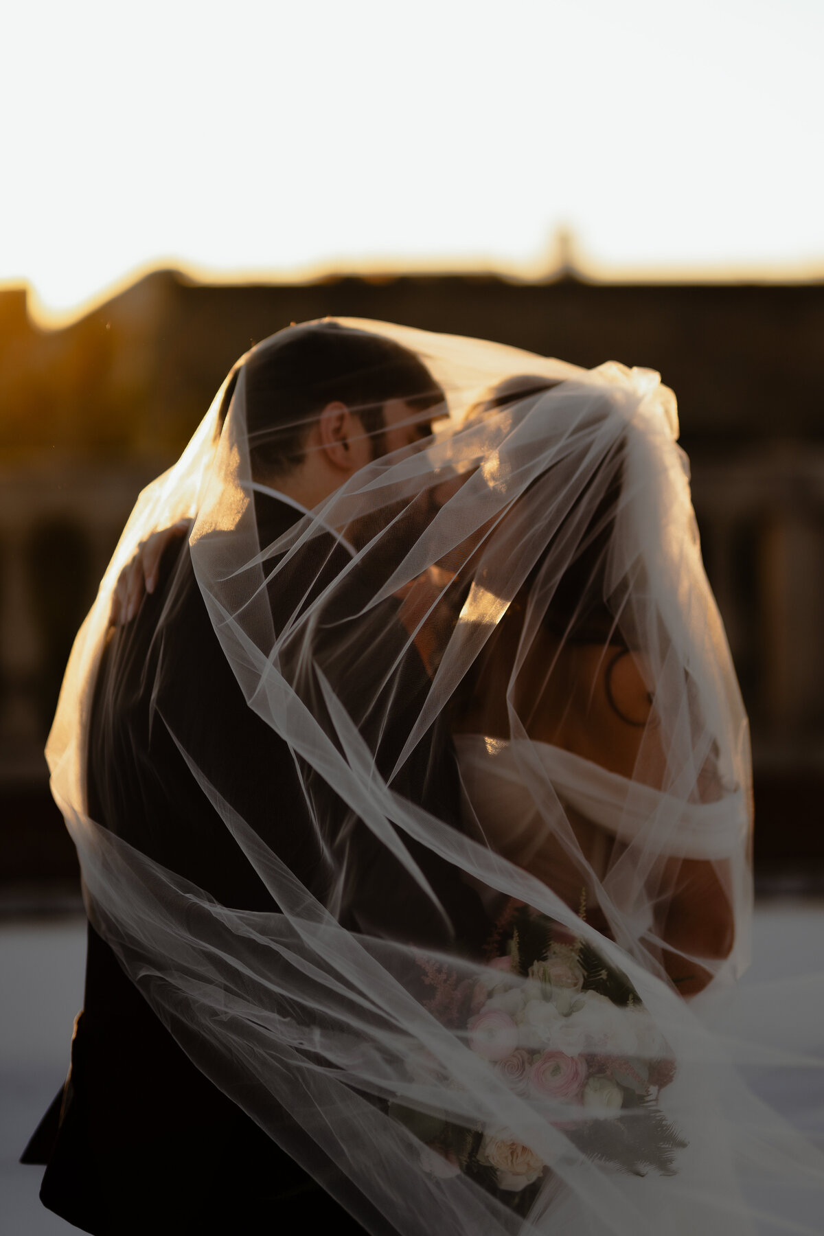 Bride and groom sharing a kiss under the brides veil at sunset.