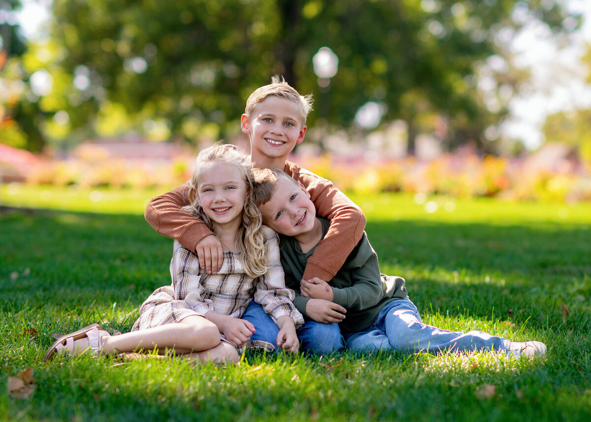 Three kids sitting together outdoors, smiling in a natural setting for their Iowa Family Portraits