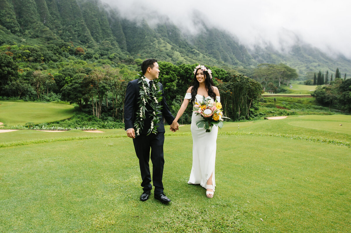 Bride and groom walk on grass with mountains in hawaii