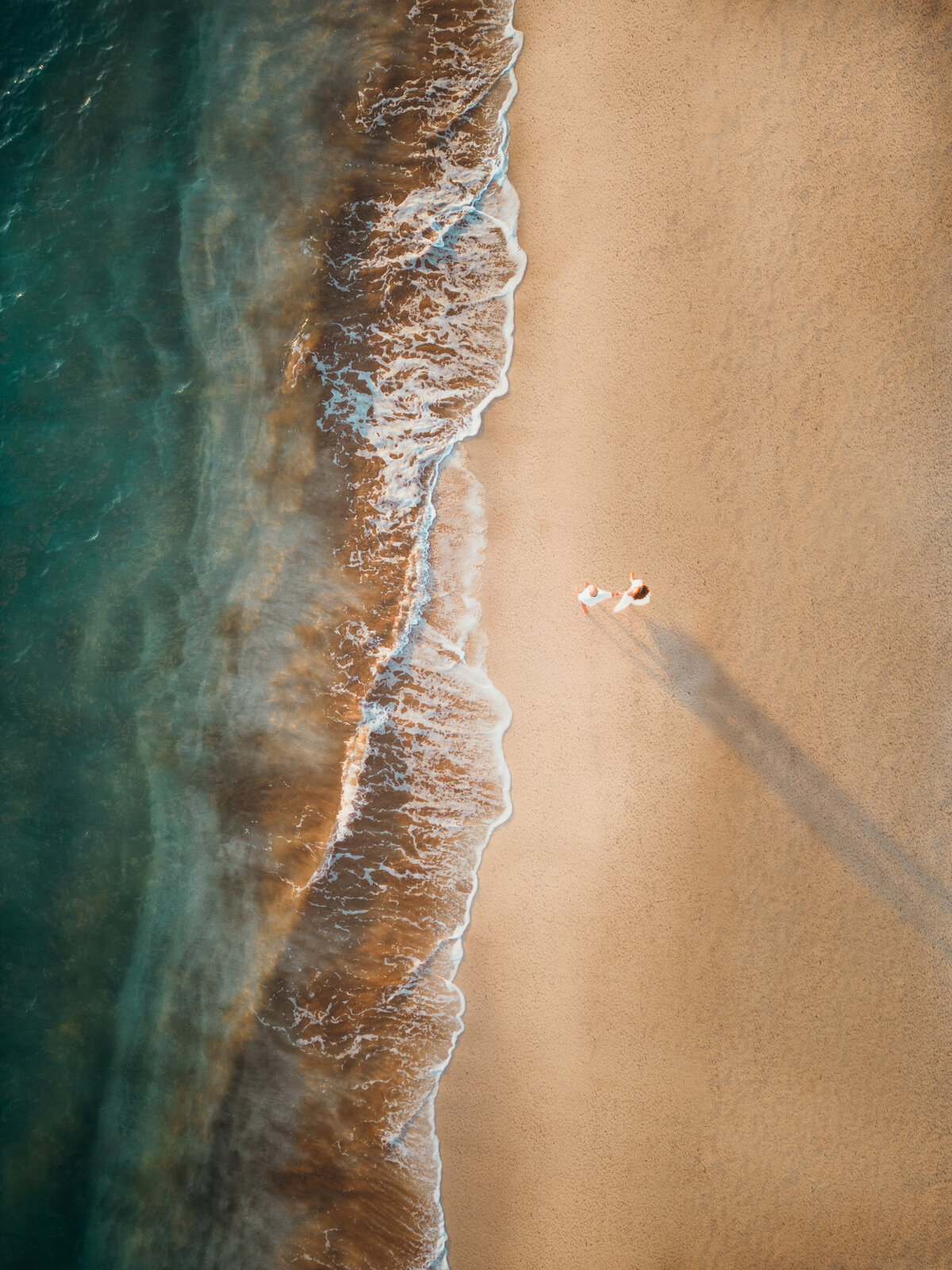 Maui Couples Photographer captures drone footage of couple walking along water during beach engagement photos