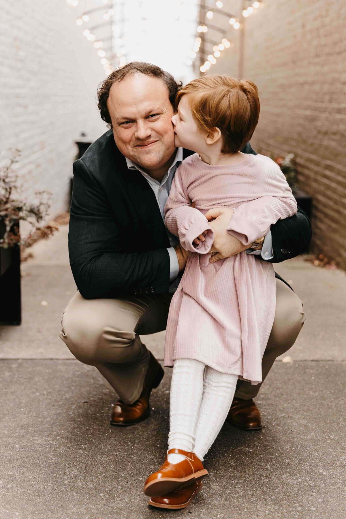 Father smiles at camera while daughter kisses him on the cheek