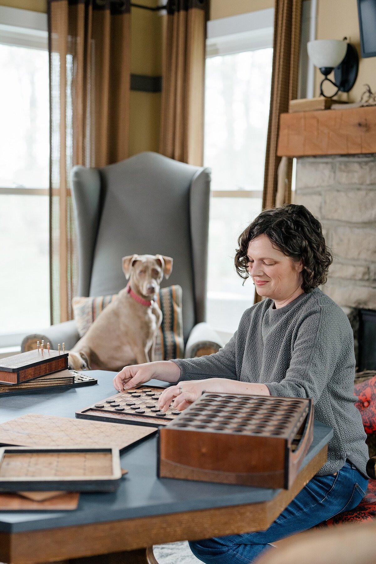 brand photographer captures woman using handmade wooden games in a living room with her dog in the background