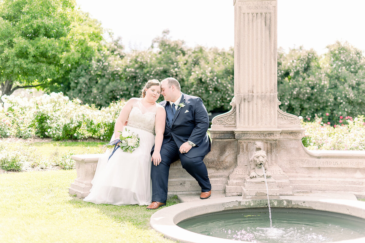 bride and groom sitting in the war memorial garden next to the water fountain foreheads together with the bride holds onto the grooms knee