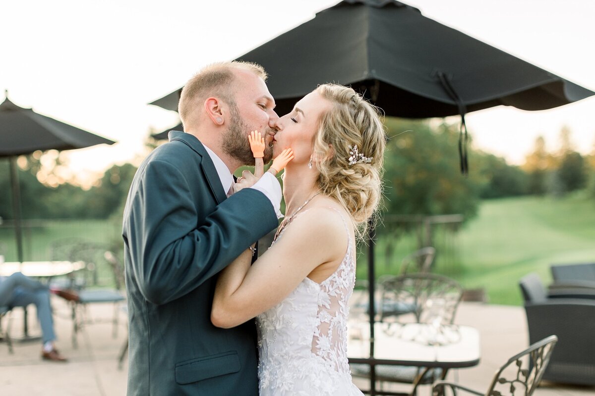 A bride and groom on a patio in  Madison, WI kissing and holding each others faces with plastic tiny hands