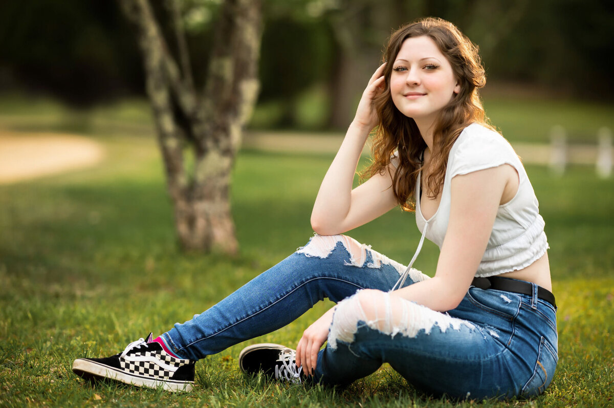Senior photo of a girl wearing rips, jeans, sitting in grass