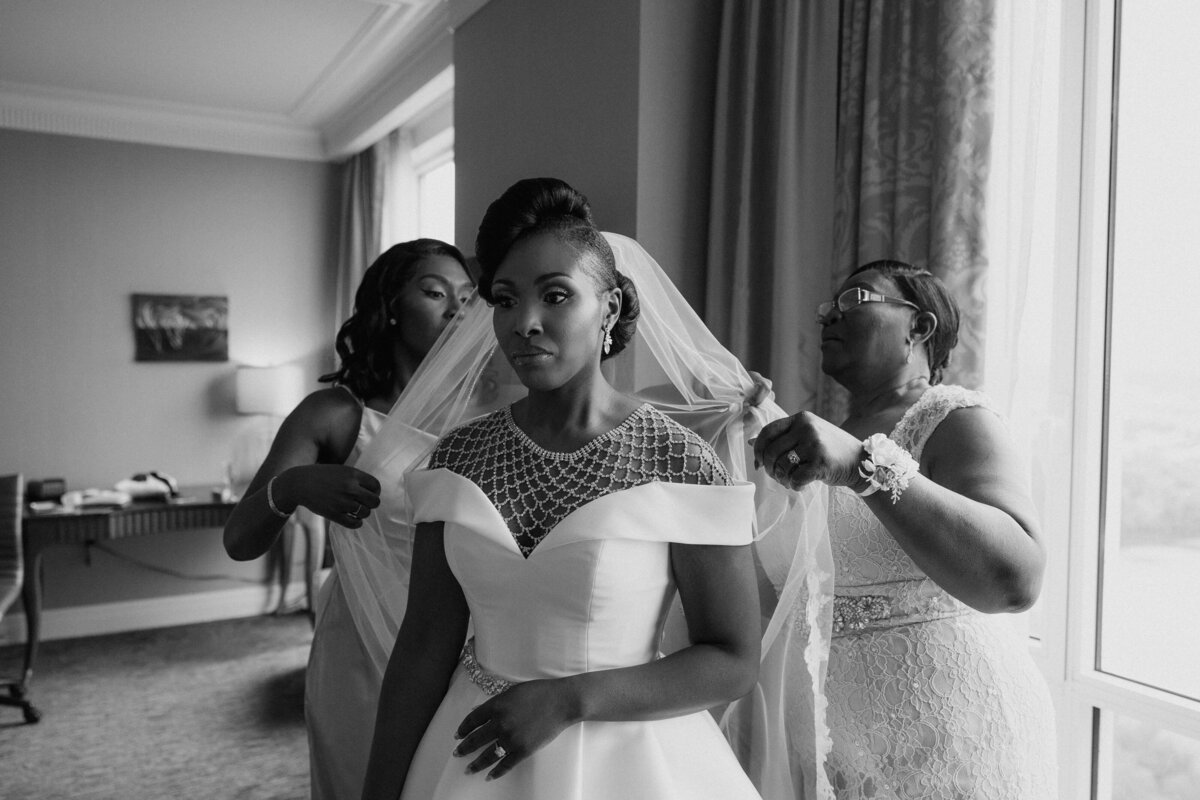 A black and white photo of the bridesmaids helping the bride fix her veil