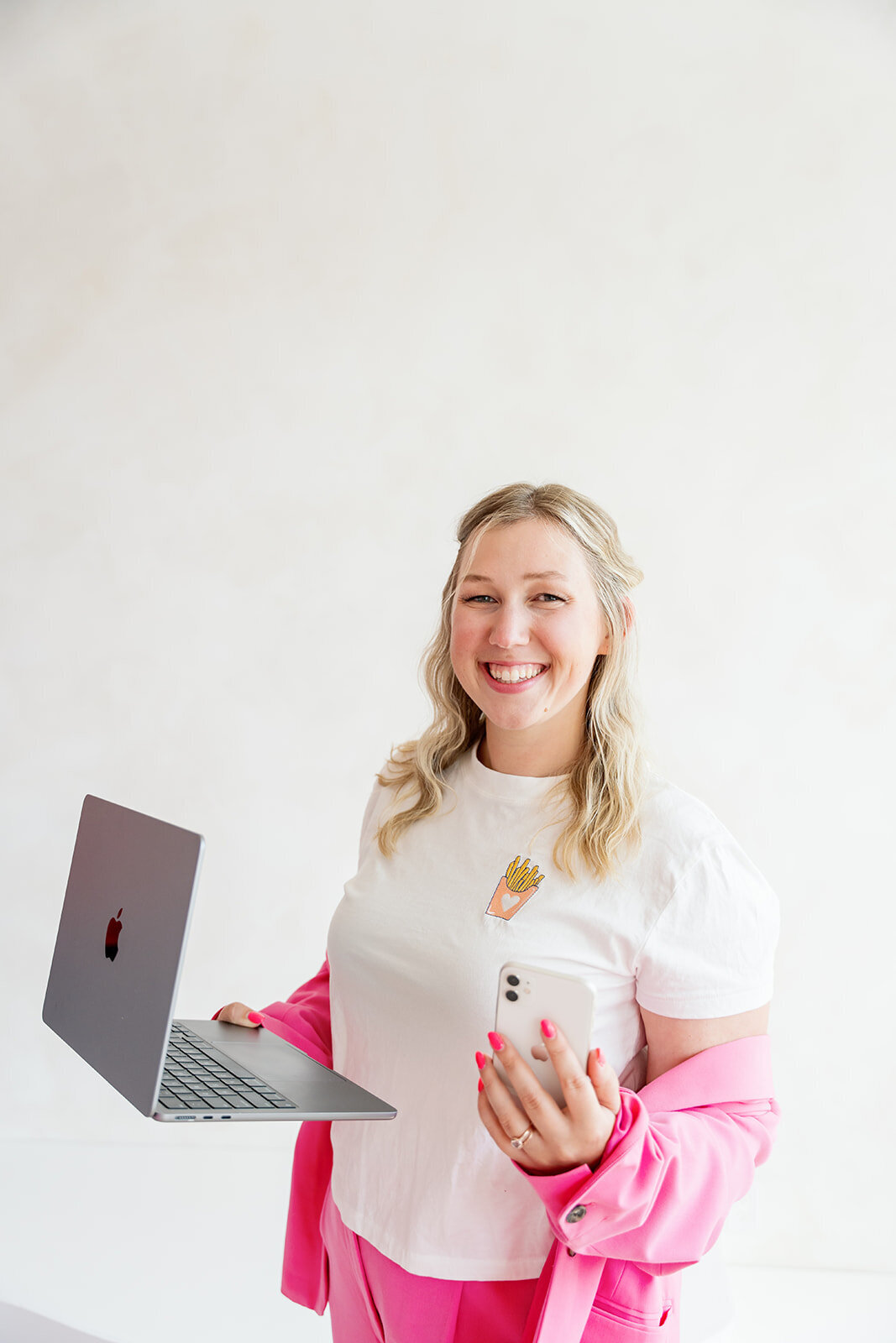 Kat Murphy in a light pink blazer flipping her hair in front of a white wall