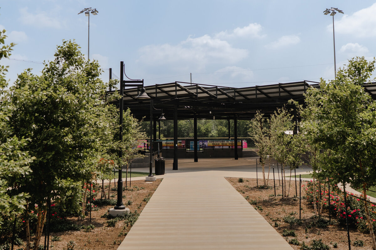 tree lined sidewalk leading to louver shade structure at baseball field park