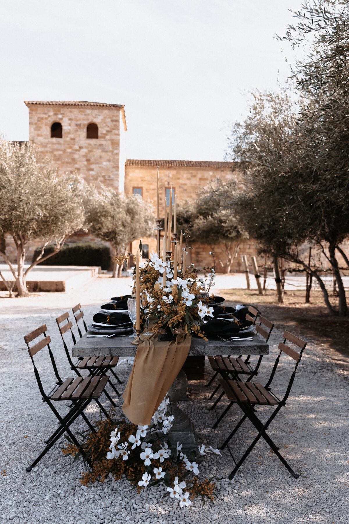 Rustic outdoor wedding reception table with black table settings, gold candles, and floral decor at Sunstone Winery in Santa Ynez, California.