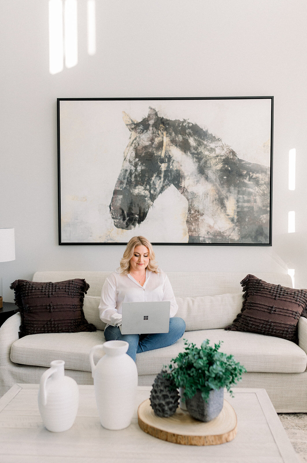 Woman works on laptop from the couch in a bright and airy room.
