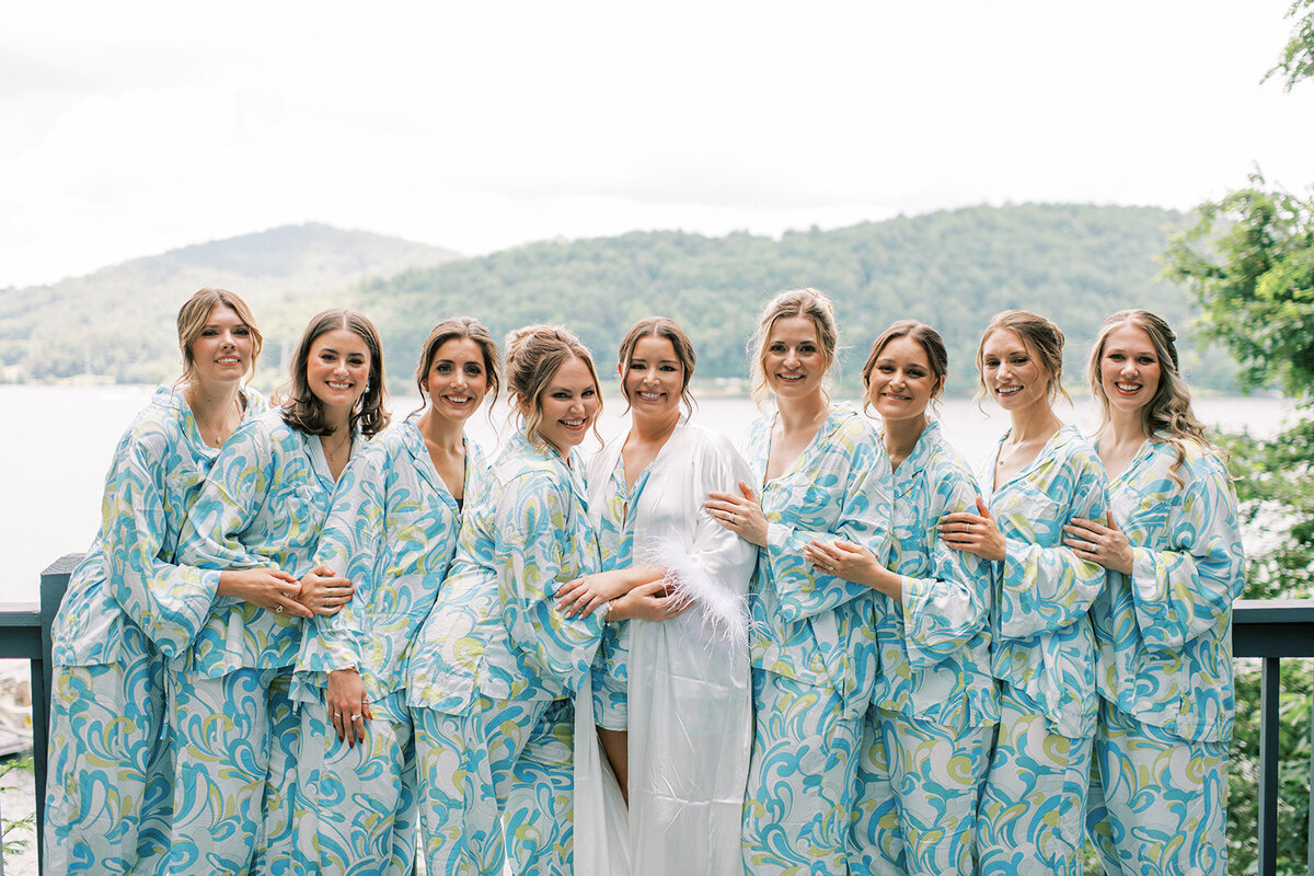 Bride and bridesmaids wearing matching blue patterned pajamas on the deck overlooking Lake Glenville.