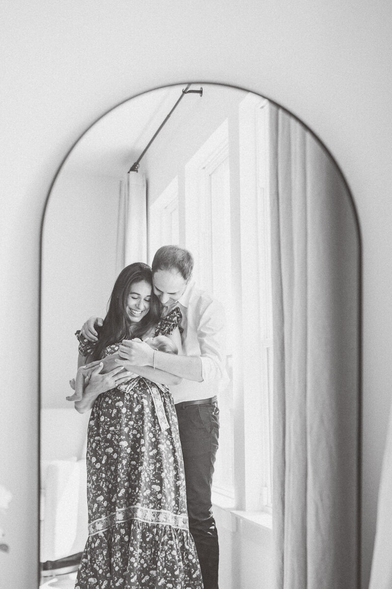 parents stand in front of a mirror in the master bedroom of their Leander home while holding and looking at their newborn.