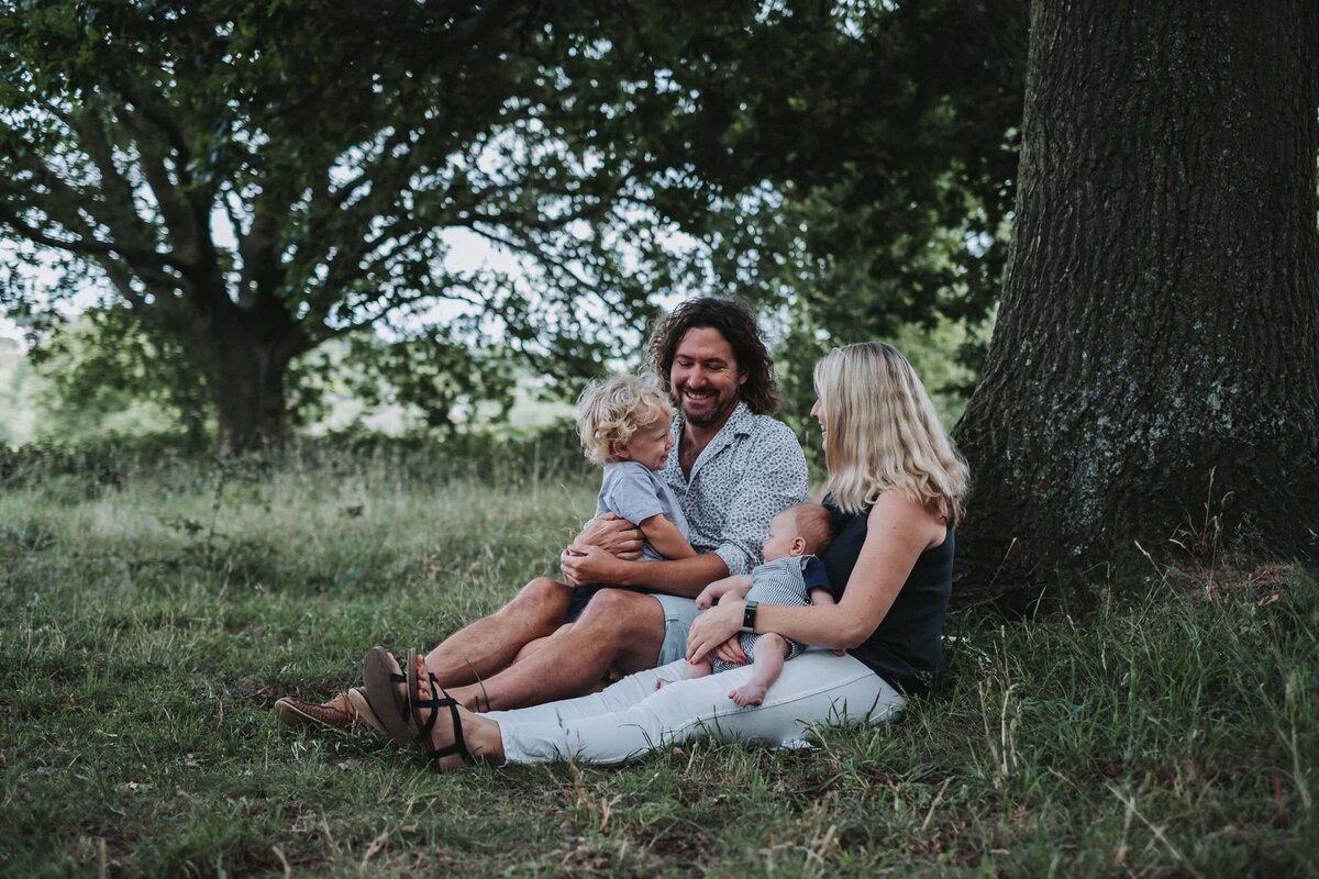 A family of four sitting on the grass next to a tree in Hampstead Heath London