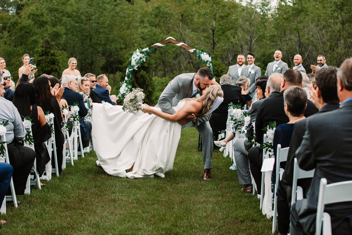 Newlyweds dip and kiss in the aisle with guests looking on