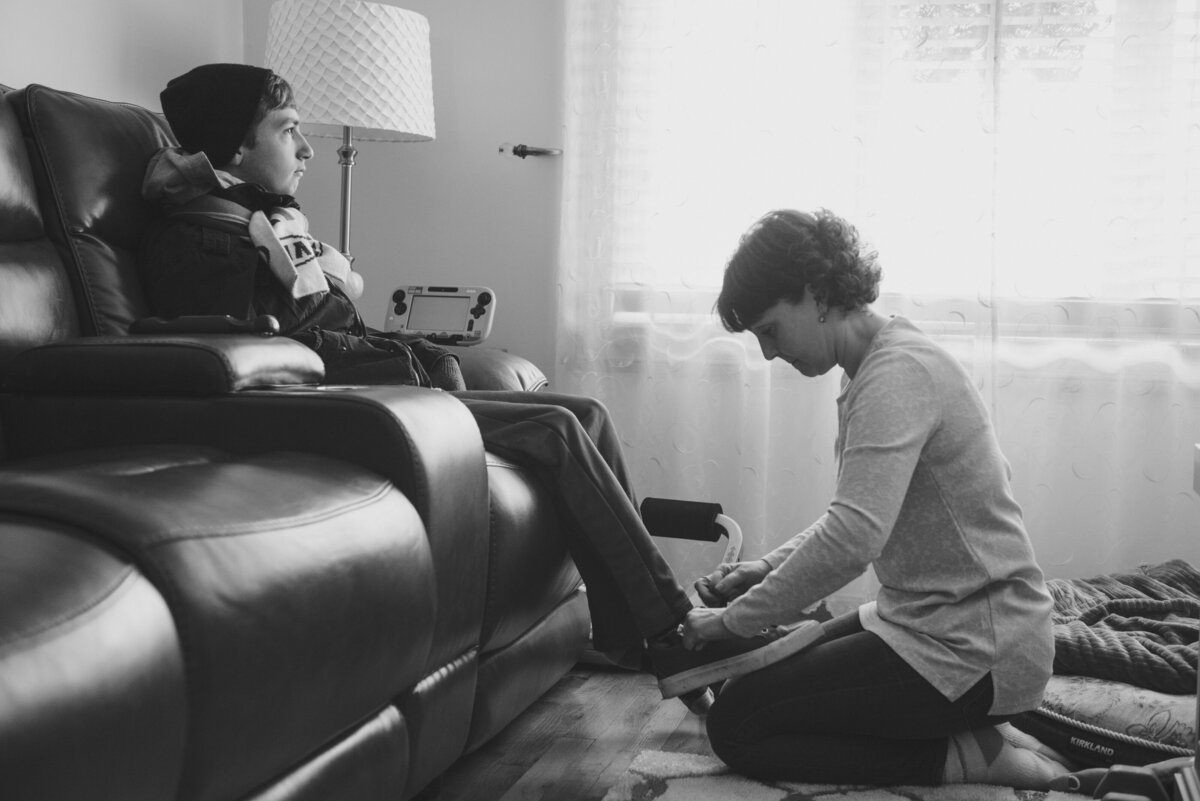A boy sitting on a couch as his mom helps put on shoes