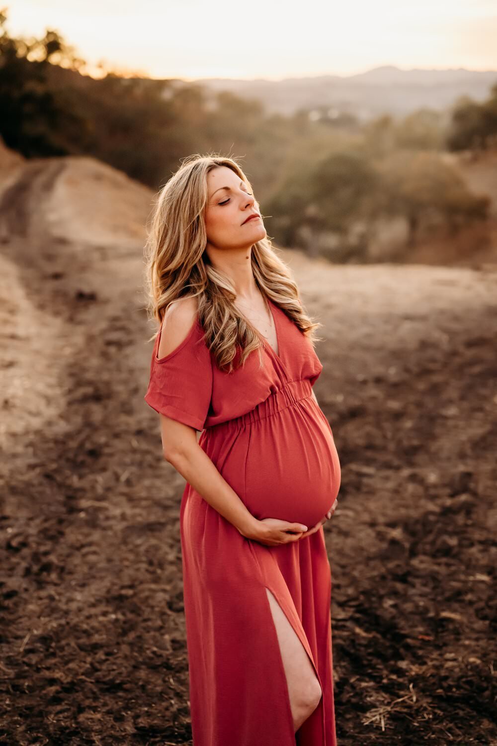 woman in pink maternity dress holds her belly and closes her eyes.