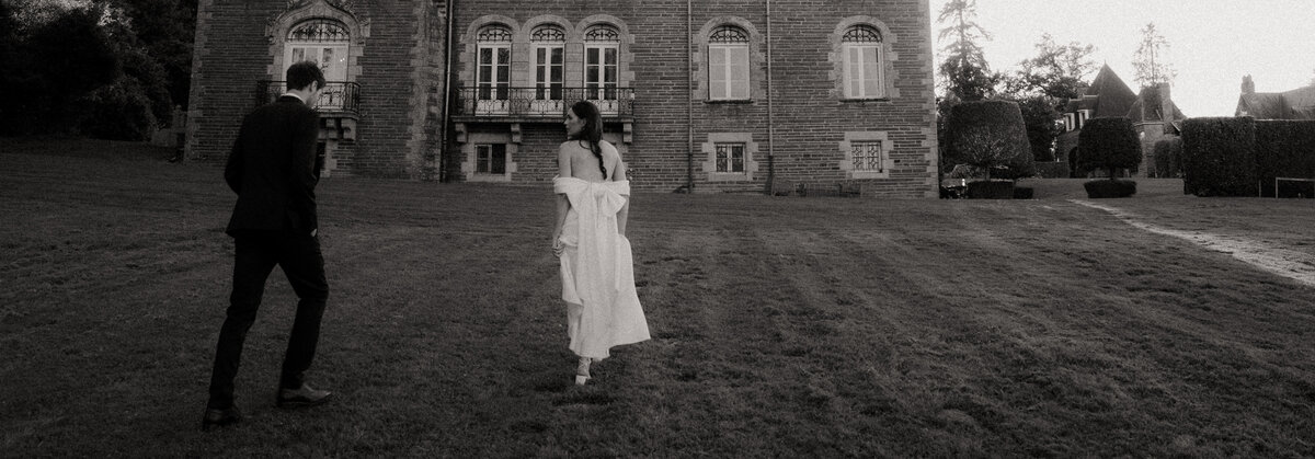 Couple de mariés, de dos, marhcant dans la pelouse en direction d'un château. Par Kamescop, vidéaste et photographe de mariage vintage.